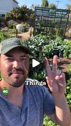 a man standing in front of a garden holding up the peace sign with his fingers