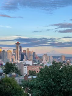 the city skyline is lit up at dusk with mountains in the distance and trees on the foreground