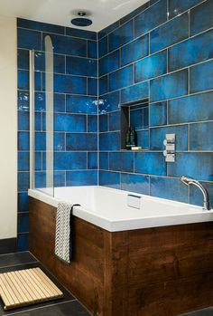 a bath tub sitting next to a shower in a bathroom under a blue tiled wall