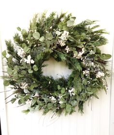 a wreath hanging on the side of a door with white flowers and greenery around it