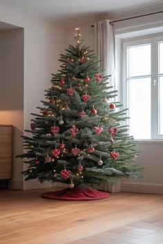 a small christmas tree with ornaments on it in front of a window and wooden floor