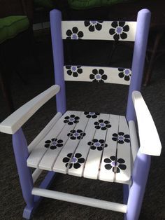 a purple and white rocking chair with flowers painted on the back, sitting in a room