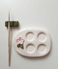 a white tray with three holes and a flower on it next to a paintbrush