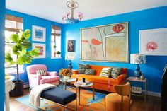 a living room with blue walls and colorful furniture in the center, along with paintings on the wall