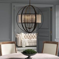 a chandelier hanging over a dining table in a room with gray walls and furniture