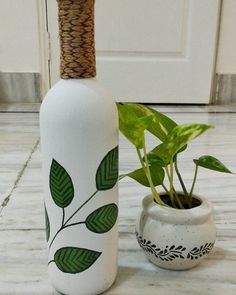 a white vase with green leaves painted on it next to a plant in a pot