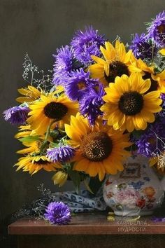 a bouquet of sunflowers and purple flowers in a white vase on a table