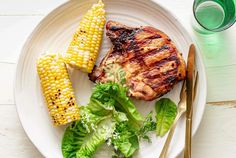 a white plate topped with meat, corn and lettuce next to a glass of water