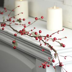 three candles are sitting on a mantle with red berries