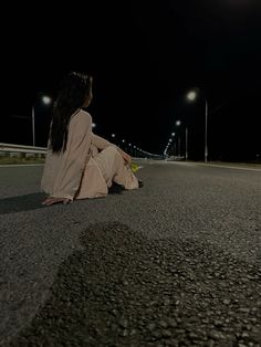 a woman sitting on the side of a road at night