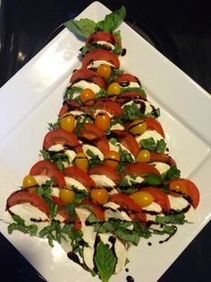 a white plate topped with a christmas tree made of tomatoes and mozzarella cheese