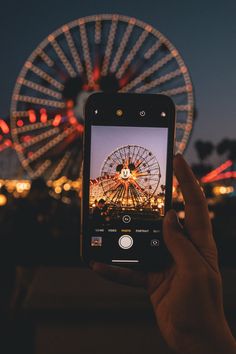 someone taking a photo with their cell phone in front of a ferris wheel at night