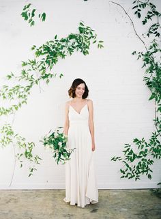 a woman standing in front of a white wall with greenery on it's sides