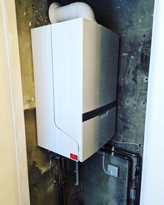 a water heater mounted to the side of a wall in a room with exposed pipes