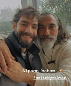 two men with long hair and beards are hugging each other in front of a window