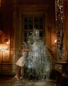 a woman standing next to a giant christmas tree in a room with lots of lights