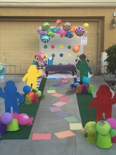 an outdoor party with paper cut out people and balloons on the ground, in front of a garage door