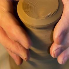 a person holding a clay pot with their hands on the potter's pottery wheel