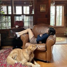 a woman sitting in a chair next to a large brown dog on top of a wooden floor