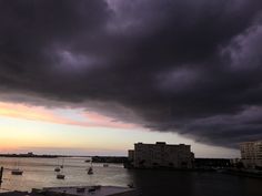 storm clouds loom over the ocean as boats sail in the water