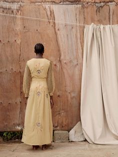 Beautiful and timeless, Hamaji’s signature flame yellow maxi dress takes inspiration from Kenya’s rich and diverse flora. Large embroidered botanical designs decorate the body of the dress, whilst the sleeves feature a more intricate pattern. Pair with burnt orange shoes to accentuate the tassels and stitch detail. Fit:This silk crepe dress has a loose silhouette with a tie-fastening at the waist and structured bell sleeves, is fully lined and features pockets. Yellow Hand Embellished Dress For Festive Occasions, Festive Hand Embellished Yellow Dress, Festive Hand-embellished Yellow Dress, Embellished Maxi Dress For Fall, Embellished Fall Maxi Dress, Festive Hand Embellished Maxi Dress, Yellow Floor-length Dress With Floral Embroidery, Bohemian Maxi Dress With Gold Embroidery, Yellow Floral Embroidered Floor-length Dress