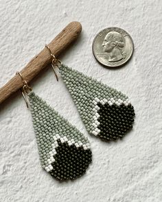 a pair of beaded earrings sitting next to a quarter penny on a white surface