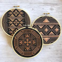 three black and gold embroidered hoops with designs on them sitting on a white wooden surface