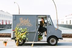 a woman sitting in the driver's seat of a food truck next to flowers