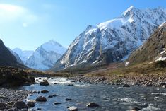 the mountains are covered in snow and rocks, along with a river running between them