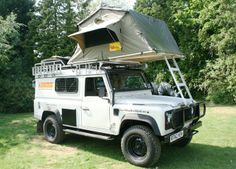 an off - road vehicle parked in the grass with a tent attached to it's roof