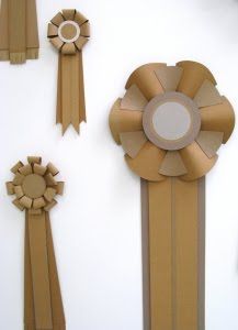 several pieces of art made out of cardboard and paper with ribbons attached to the wall