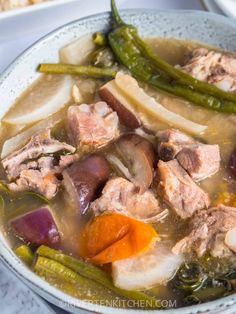 a white bowl filled with meat and vegetables on top of a table next to bread