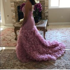 a woman in a long pink dress is standing near a fire place and looking at the fireplace