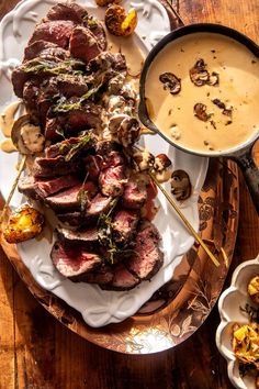 steak with mushroom sauce and mushrooms on a platter next to a bowl of soup