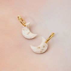 two white and gold moon shaped earrings on a pink background