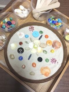 an assortment of seashells in plastic containers on a wooden tray with spoons and utensils