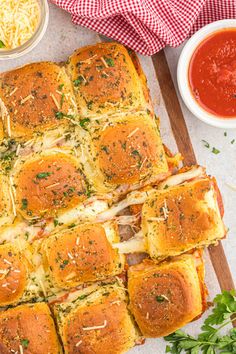 a wooden cutting board topped with rolls covered in cheese and toppings next to bowls of sauce