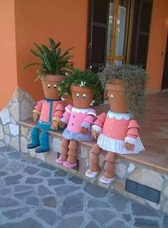 three little dolls sitting on the ledge of a stone wall with potted plants in front of them