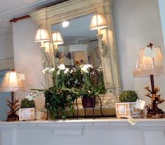 a mantle with flowers and candles on it in front of a mirror above the fireplace