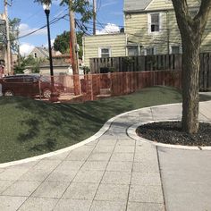 a backyard with grass and trees in the back yard, next to a sidewalk that has a car parked on it