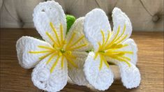 a crocheted white flower with yellow stamens on a wooden table top