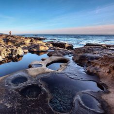 a man standing on top of a rocky beach next to the ocean with large holes in it