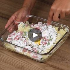 someone is adding ingredients to a casserole in a glass dish on a wooden table