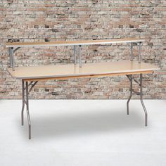 a wooden table sitting in front of a brick wall with two metal shelves on it