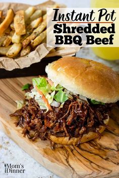 the instant pot shredded bbq beef sandwich on a wooden cutting board with french fries