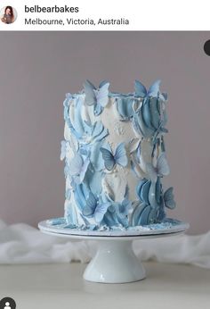 a blue and white cake with butterflies on it's top is sitting on a table