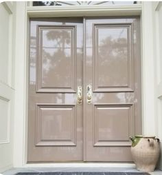 the front door to a house with two large doors and a vase on the side