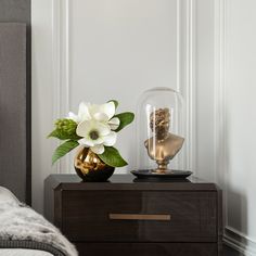 a gold vase with flowers on top of a wooden dresser next to a white wall