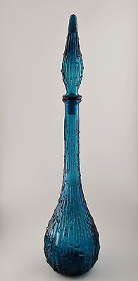 a tall blue glass vase sitting on top of a table next to a white wall