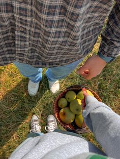 two people standing next to each other in the grass with fruit in a basket on their feet